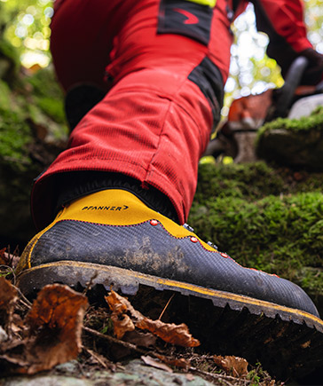 Gros plan sur une chaussure de s�curit� noire avec des d�tails jaunes sur le sol forestier.